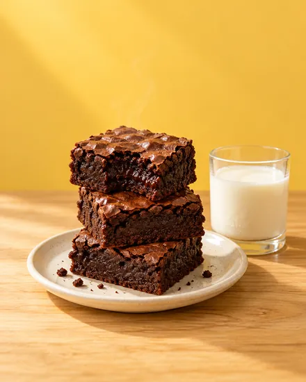 Tres brownies húmedos apilados junto a un vaso de leche